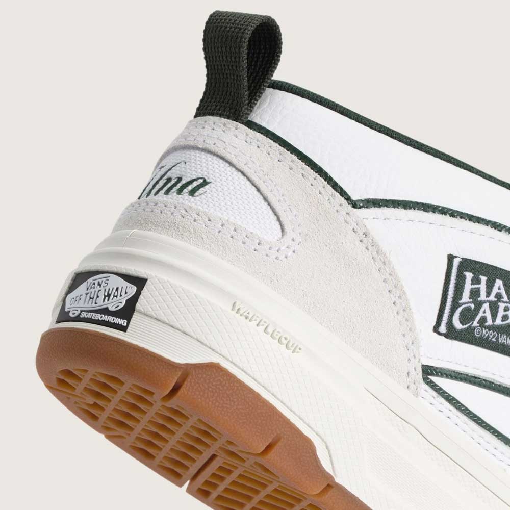 Close-up of the heel on Vans Skate Half Cab Walnut Gum VN0A5FCD77J1 Suede Skateboard Shoes, featuring green trim, cream suede details, black pull tab, brown rubber sole, Vans Off The Wall logo on the heel, and PopCush impact protection for comfort.