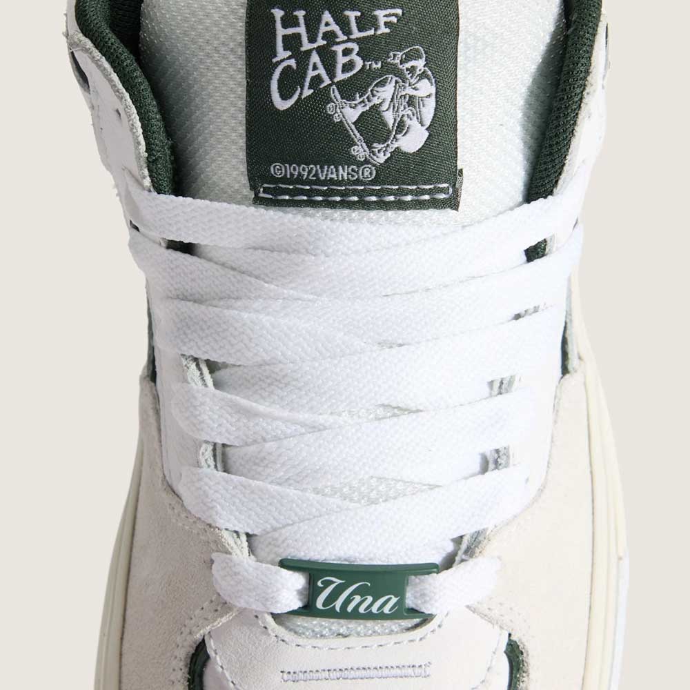 Close-up of the Vans Skate Half Cab Walnut Gum VN0A5FCD77J1 suede skateboard shoe in white with white laces. The tongue label has the Half Cab logo and skate graphic; PopCush impact protection adds comfort. Bottom lace tag reads "Una" in script.