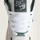 Close-up of the Vans Skate Half Cab Walnut Gum VN0A5FCD77J1 suede skateboard shoe in white with white laces. The tongue label has the Half Cab logo and skate graphic; PopCush impact protection adds comfort. Bottom lace tag reads "Una" in script.