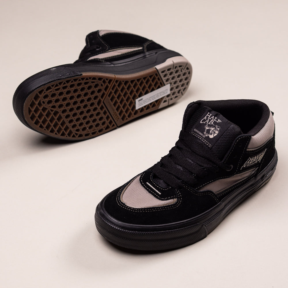 A pair of Vans Wafflecup Half Cab Black Peyote VN000D9ZOUK1 Suede Skate Shoes—one upright and one on its side highlighting the WaffleCup gum sole—are displayed on a light beige background, showcasing their durability and style.