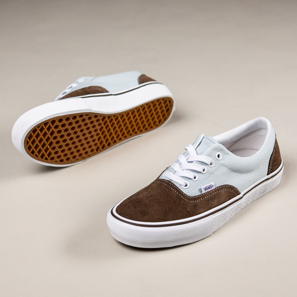 The Skate Era Brown Blue VN000ECRCL11 Vans feature low-top design, brown suede on toe and sides, light blue canvas uppers, white laces, white soles, and gum rubber waffle outsoles with advanced skate tech for impact protection.