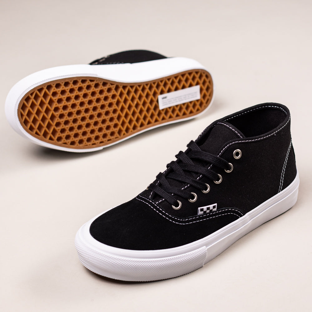 The VN0000EEQY281 Suede Black Authentic Mid Vans Skate Shoes feature white rubber soles, white stitching, and a brown waffle-patterned tread—one shoe stands upright while the other lies on its side; classic skate style.