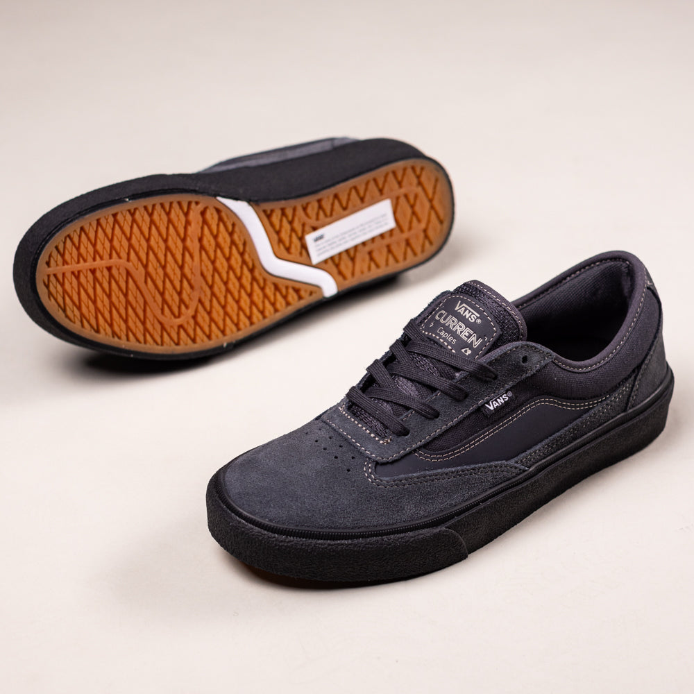 A pair of VN000D85CC81 Skate Curren Caples Charcoal Black Vans suede and rubber shoes, one upright and one showing the brown, textured sole with a white stripe pattern.