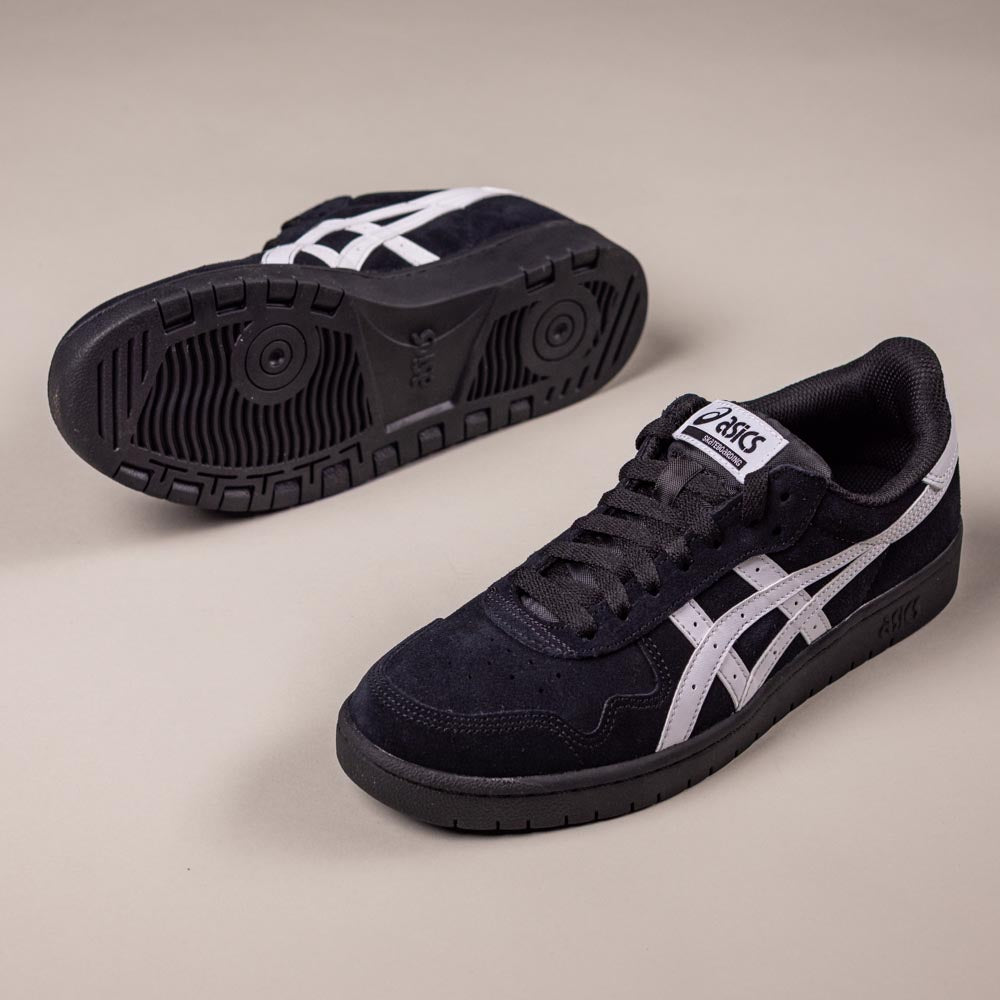 A pair of Japan Pro Asics Black White 1201A92001 Suede Skateboarding Shoes—one upright showing side and laces, the other on its side revealing the sole—are displayed on a plain, light-colored surface.