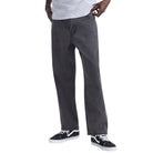 Someone wearing Vans Loose Denim Black VN000PH6BLK Skate Check 5 Pants, a light gray t-shirt, and black and white sneakers stands with one hand in their pocket against a plain background.