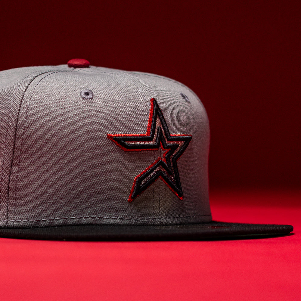 A Days B4 WS05 Misty Black Houston Astros New Era 5950 Fitted Hat featuring a gray and Misty Black colorway with a black and red outlined star logo on the front, showcased against a vibrant red background.