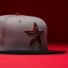 A Days B4 WS05 Misty Black Houston Astros New Era 5950 Fitted Hat featuring a gray and Misty Black colorway with a black and red outlined star logo on the front, showcased against a vibrant red background.