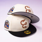 Two cream and black baseball caps, including the Warren 2.0 Hooks Chrome Black New Era Hat 5950 Fitted, feature embroidered fishing hooks and ocean patches; one hat is stacked on top of the other, both set against a light purple gradient background.