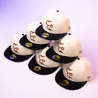 Six cream-colored Warren 2.0 Hooks Chrome Black New Era Hat 5950 Fitted caps, each featuring a sleek black brim and a stylized script logo on the front, are arranged in a pyramid formation against a gradient white-to-purple background—an elevated display of this exclusive New Era collection.