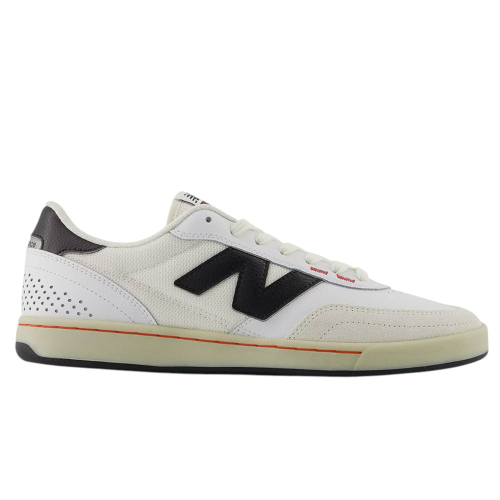 The White Black 440 NO2 New Balance Numeric Suede Skateboarding Shoes are white low-top sneakers featuring a black New Balance “N” logo, a black heel accent, white laces, and a beige sole with an orange stripe along the edge. Built for durability as a skate shoe, they include an ABZORB midsole that provides extra comfort and impact protection.