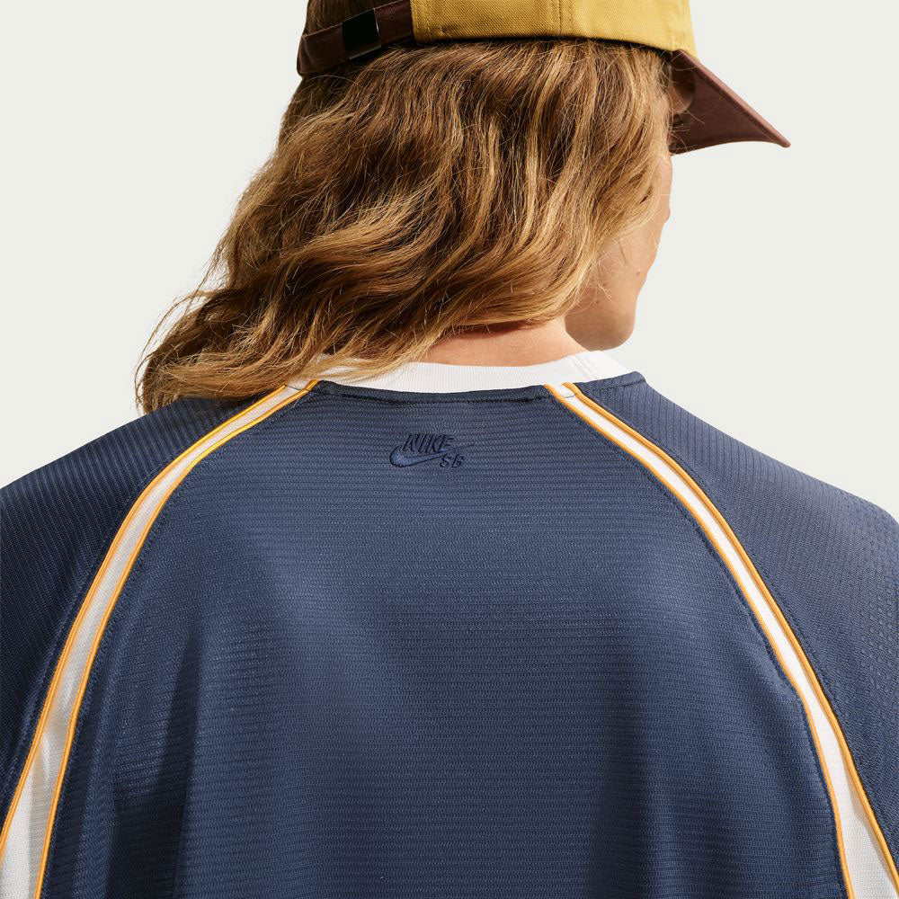 A person with long hair wears a brown cap and the Nike SB Yuto 1 Jersey Navy IM5465-437, shown from the back.