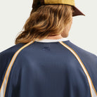 A person with long hair wears a brown cap and the Nike SB Yuto 1 Jersey Navy IM5465-437, shown from the back.