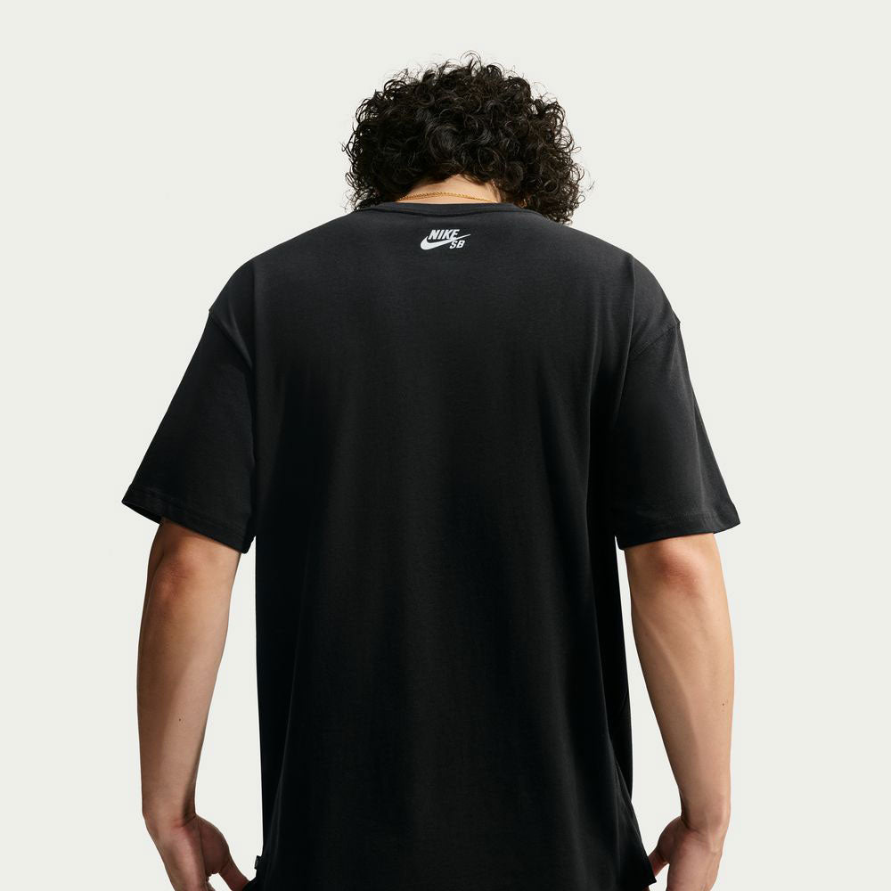Person with curly hair wearing a black Nike SB Yuto 1 Tee (IM4432-010), seen from behind. The sweat-wicking skateboarding t-shirt features the Nike SB logo printed in white near the neckline on the back. The background is plain and light-colored.