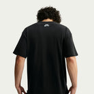 Person with curly hair wearing a black Nike SB Yuto 1 Tee (IM4432-010), seen from behind. The sweat-wicking skateboarding t-shirt features the Nike SB logo printed in white near the neckline on the back. The background is plain and light-colored.