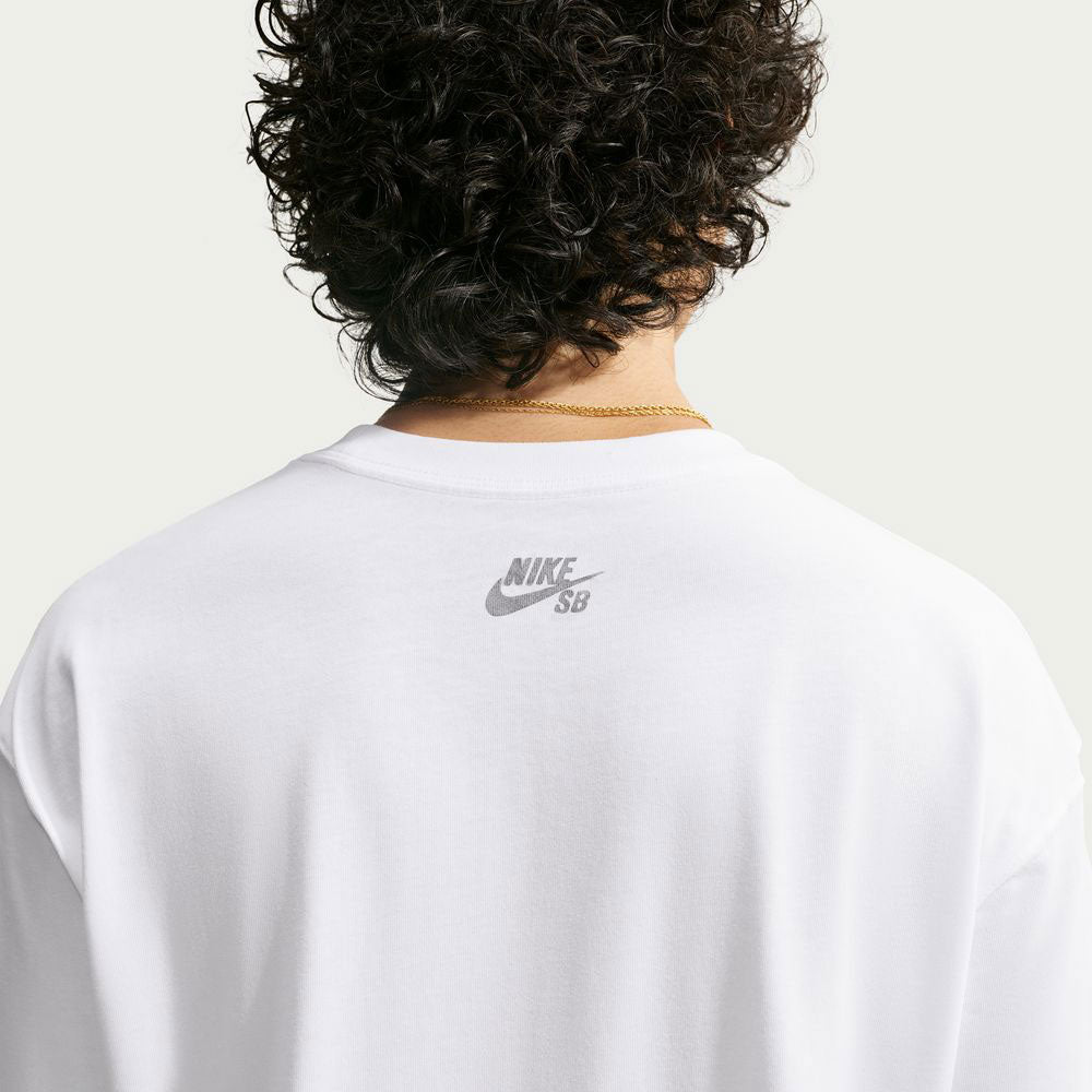 A person with curly hair is shown from the back wearing the white Yuto 1 Tee (IM4432-100), a Nike SB Skateboarding T-shirt, paired with a visible gold chain necklace. The Nike SB logo appears near the neckline of this sweat-wicking skate top. The background is plain and light-colored.