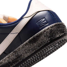Close-up of the heel of a blue void and sail Zoom Tennis Classic x Rassvet IO9846400 Nike SB leather skateboarding shoe, featuring a textured, slightly worn black-and-white sole and an embossed geometric logo near the heel.