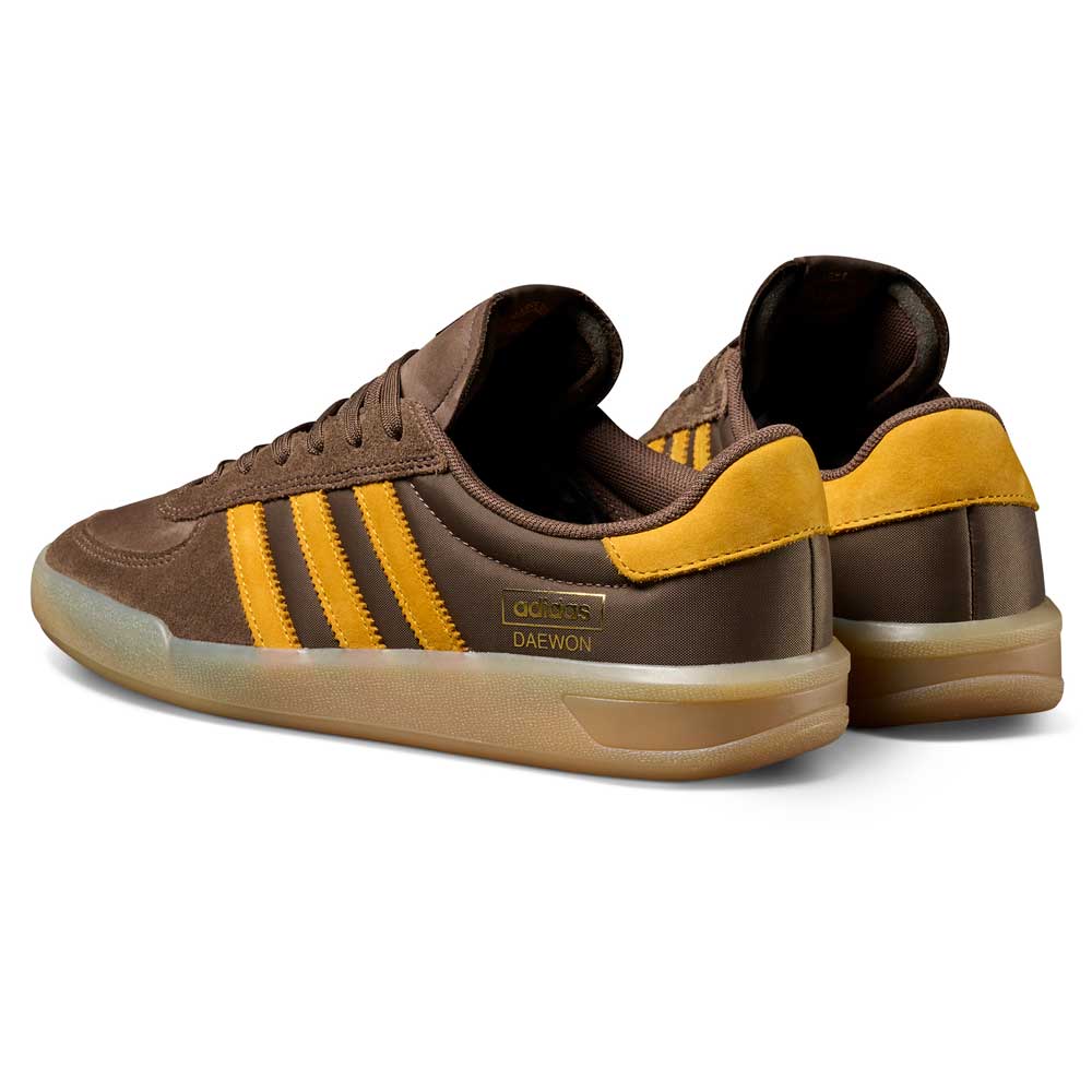 Daewon Song Glenburn Brown Yellow KZ8777 Adidas Skateboarding Shoes featuring a brown upper with yellow stripes and accents, gum soles, and “DAEWON” printed in gold on the side. These iconic skateboarding shoes are displayed at an angle to showcase both the outer and rear views.