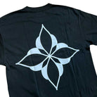 Introducing the Cleo Icon Black Tee—a black t-shirt showcasing a bold, white geometric flower-inspired design with four pointed petals on the back. Expertly crafted for the perfect fit using meticulous cut-and-sew construction, this tee merges contemporary style with superior craftsmanship.