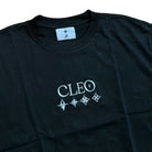 The Cleo Icon Black Tee features the word “CLEO” and four distinct star-like symbols printed in white across the front. Designed with cut-and-sew construction for an optimal fit, this black T-shirt also includes a white logo tag inside the collar.