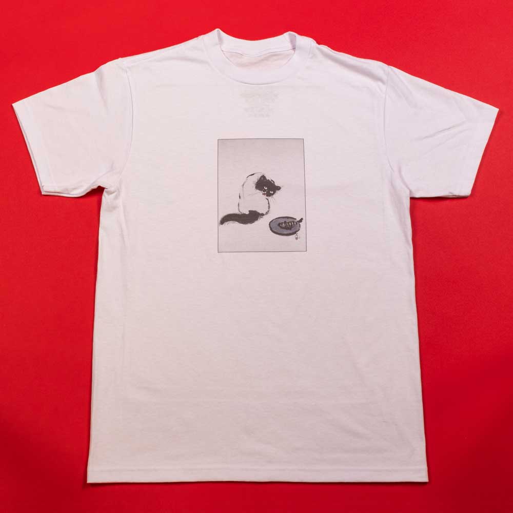 The Curious Cat Southside White Tee by Nguyen Duc Hien is a classic fit, white USA cotton shirt with a black and white cat illustration centered on the chest, showing the cat eyeing a bowl. Displayed on red, it blends comfort and style.