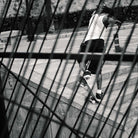A person in a white shirt and shorts skateboards down concrete steps in Superskate x Kader Shoes JQ4413 Core Black/Off White Leather Suede Adidas Skateboarding Shoes—dynamic black and white photo seen through blurred metal bars.