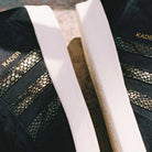 Close-up of two adidas Superskate x Kader Shoes (JQ4413) in core black with off-white soles, gold KADER text, a suede and leather upper, and reptile-scale-patterned stripes on the sides.