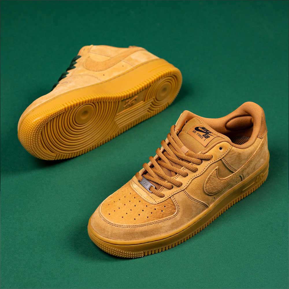 A pair of Nike SB Air Force 1 Flax Black sneakers with suede uppers and rubber soles are displayed on a green background—one flat, one on its side—ideal for your next READ BELOW the BUTTON RAFFLE entry at Southside Skatepark.