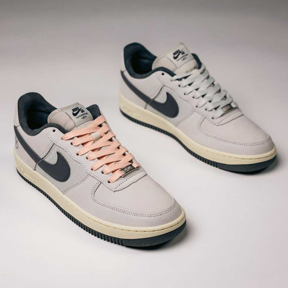 A pair of Yuto AF1 Iron Grey White Coconut Milk IO8439100 Nike SB Suede Skateboarding Shoes with black swooshes; the left shoe features pink laces, and the right shoe has white laces. Designed as premium skate shoes, both have dark soles, Nike Air cushioning for enhanced comfort, and are presented on a light background.