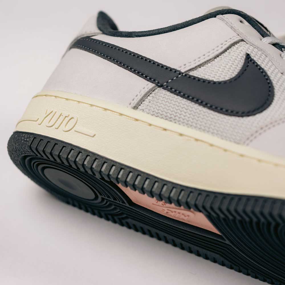 Close-up of the Yuto AF1 Iron Grey White Coconut Milk IO8439100 Nike SB Suede Skateboarding Shoe’s heel, showcasing the black Nike Swoosh, light gray suede upper, and off-white midsole embossed with “YUTO.” A black outsole and Nike Air cushioning combine classic skate-inspired details with all-day comfort.