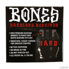 A black box of Bones Hardcore Bushing Hard Black with bold white and red text highlights high rebound, smooth turning, better centering, no break-in time, and no stretching. "HARD" is emphasized in red.